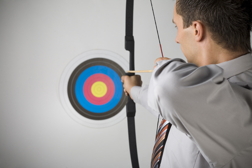 Businessman holding bow and shooting to archery target. Rear view, gray background